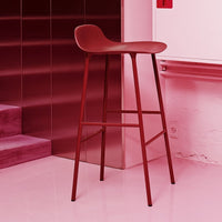 Red modern bar stool with a sleek design, featuring a smooth surface and minimalist style against a pink backdrop.