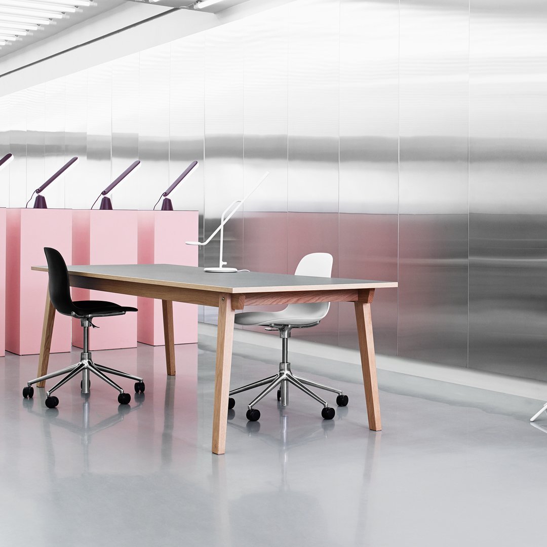 Modern office setup featuring black and white chairs, a light wooden table, and pink background accents against a metallic wall.