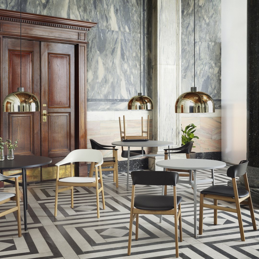 Elegant black, white, and natural wood dining chairs on a bold geometric patterned floor with marble accents.