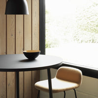 Black round table with a matte finish, light wood paneling, and a soft beige chair featuring a minimalist design.