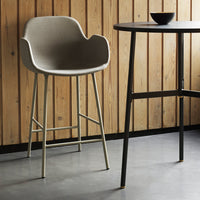 Gray upholstered bar stool with minimalist design, paired with a black table against a warm wooden backdrop.