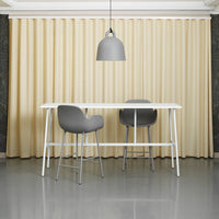 Beige curtains softly draping behind a modern white table and gray bar stools in a sleek, minimalist setting.