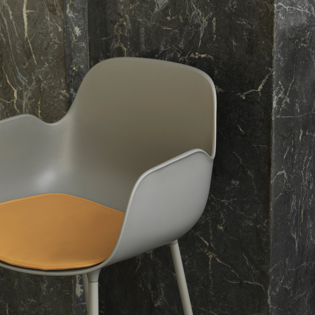 Gray chair with a smooth finish and a warm orange seat, set against a dark marble backdrop.