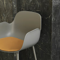 Gray chair with a smooth finish and a warm orange seat, set against a dark marble backdrop.