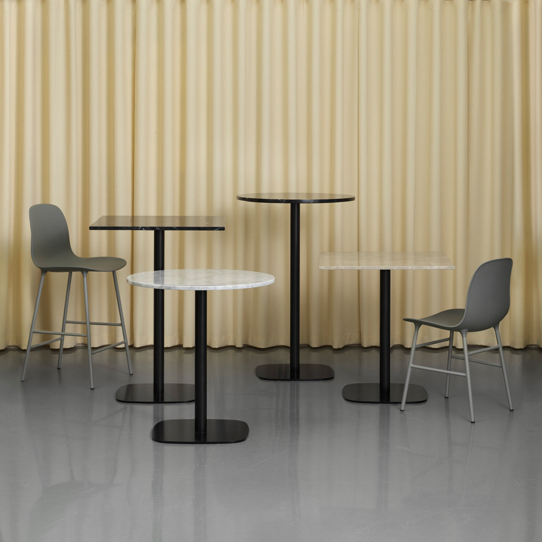Set of modern tables with black bases, white and black tops, and gray chairs against a soft beige curtain backdrop.