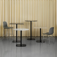 Set of modern tables with black bases, white and black tops, and gray chairs against a soft beige curtain backdrop.