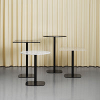 Four modern tables featuring black and white surfaces with sleek bases, set against a soft cream curtain backdrop.
