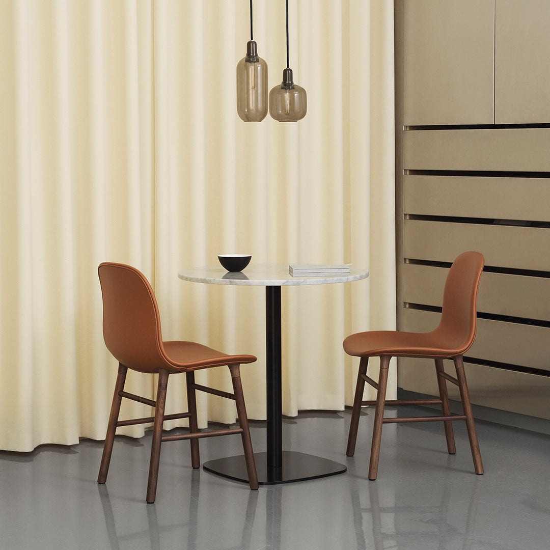 Brown chairs with wood legs paired with a sleek white table, set against soft yellow curtains and a minimalist backdrop.