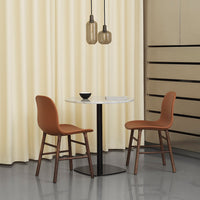 Brown chairs with wood legs paired with a sleek white table, set against soft yellow curtains and a minimalist backdrop.
