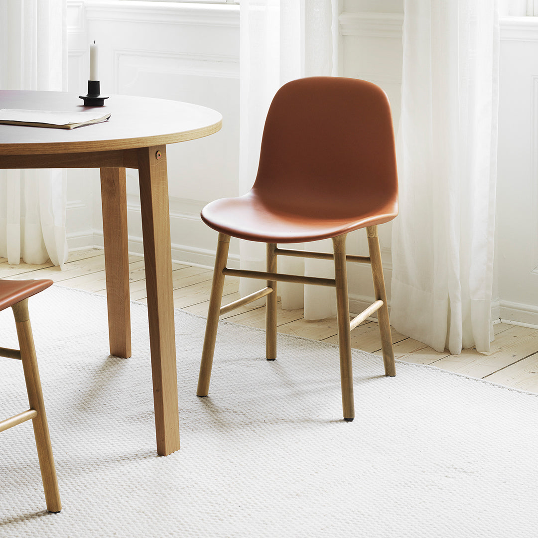 "Modern chair in earthy terracotta with natural wood legs, set against a light, minimalist backdrop."