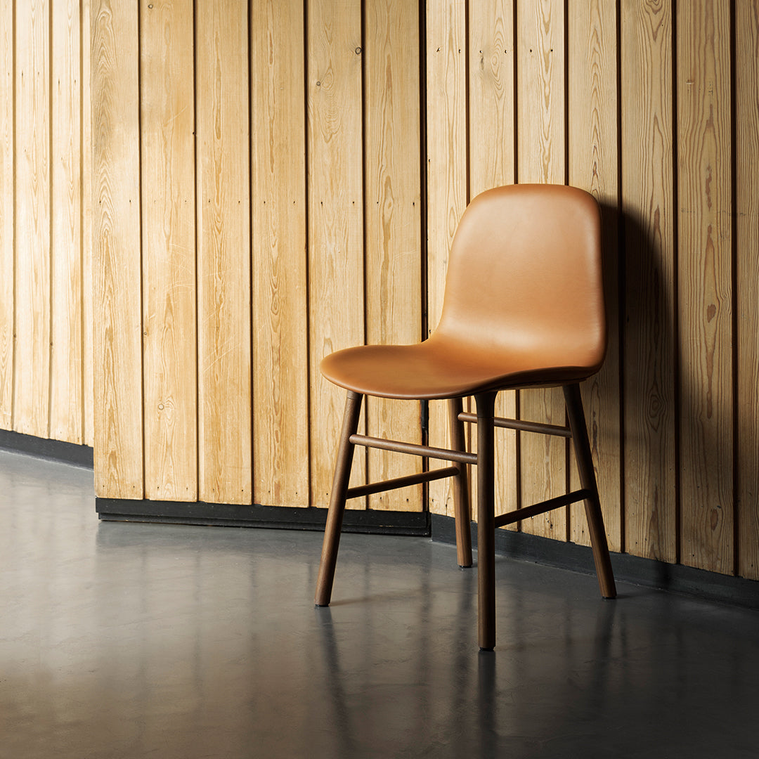Tan chair with a smooth surface and wooden legs against a backdrop of natural wood paneling and gray flooring.