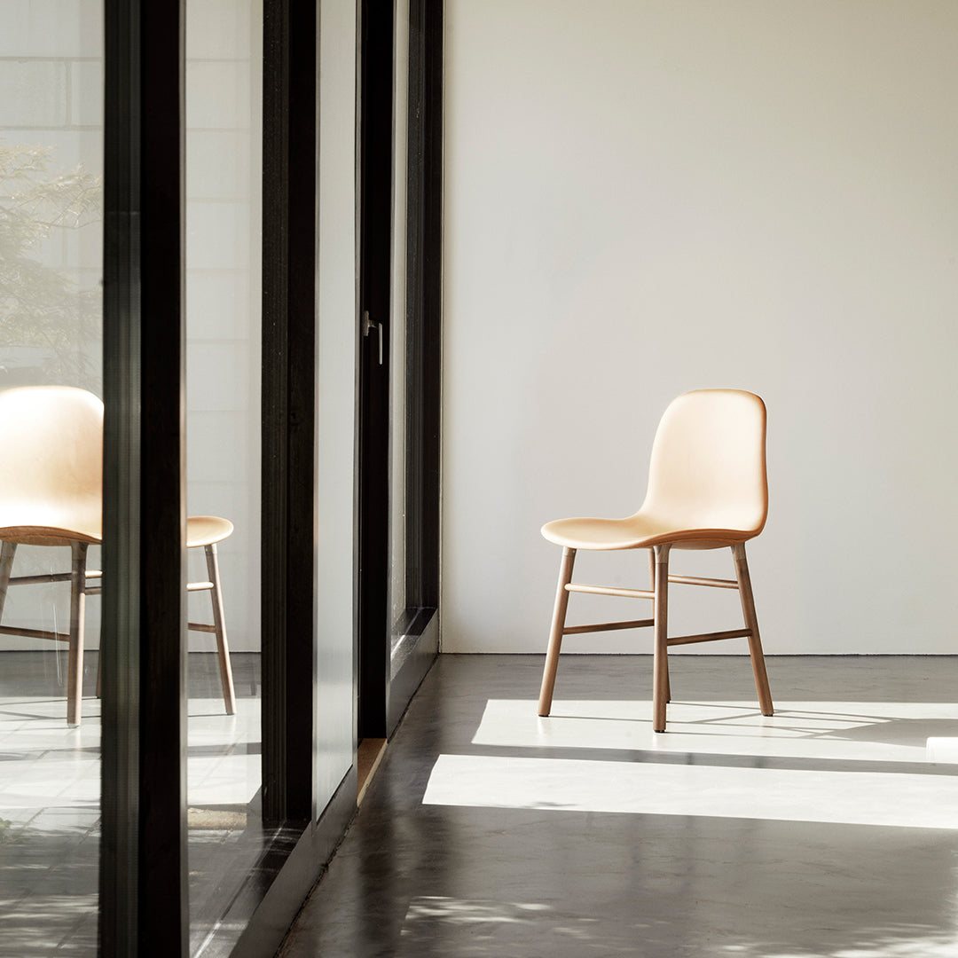 "Minimalist beige chair with wooden legs, showcasing a smooth surface in a bright, airy setting."