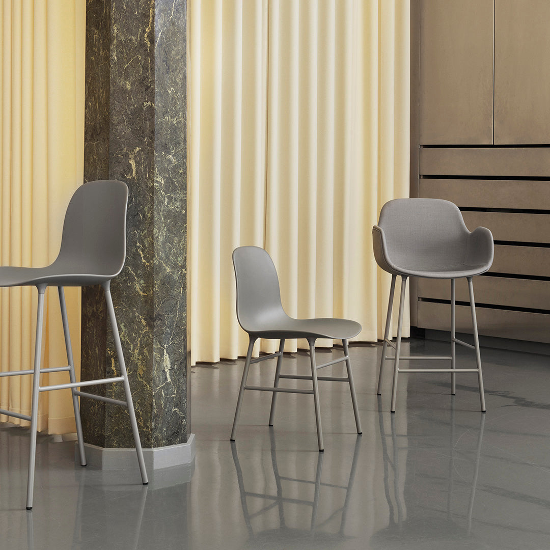 Gray bar stools and a chair against a beige backdrop with vertical pleats, highlighted by a marble pillar.