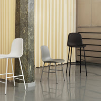 Three minimalist chairs in white, gray, and black hues, featuring smooth lines and modern design.