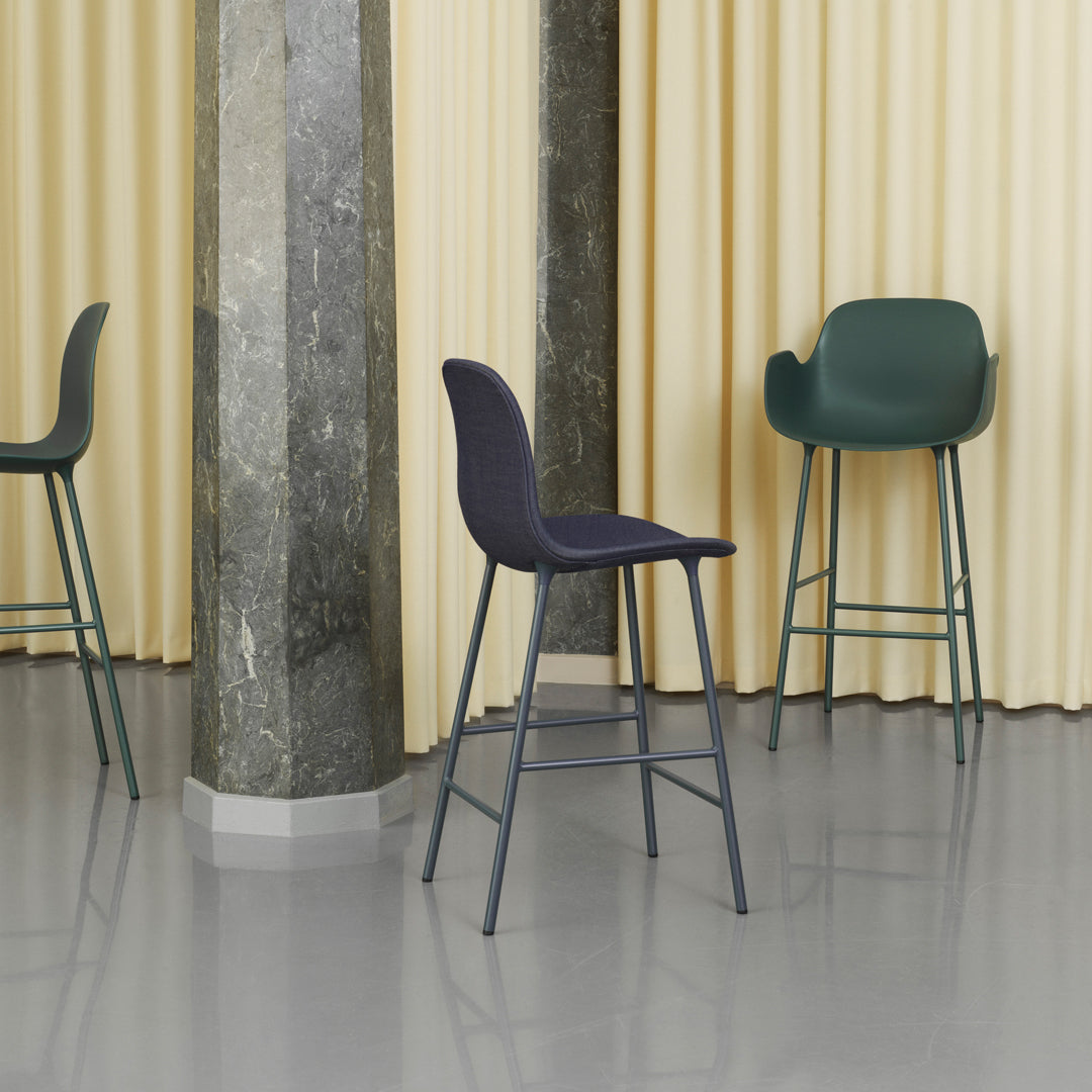 Elegant black and green bar stools against soft yellow curtains and a polished gray floor. Modern design, minimal pattern.