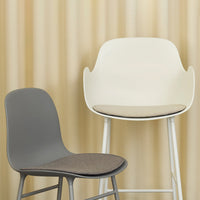 Two modern chairs: one sleek gray with a fabric seat, and a white high chair with a minimalist design, set against beige vertical stripes.