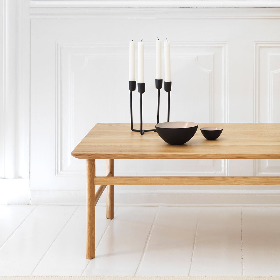 Natural wood table with a smooth finish, featuring black candlesticks and bowls for a modern contrast in a bright setting.