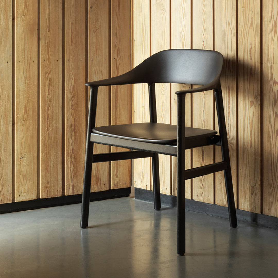 Black armchair with a minimalist design, featuring smooth curves and a matte finish, set against wooden walls.