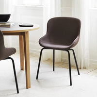 Brown upholstered chair with smooth curves and black metal legs, set in a bright, minimalist dining space.