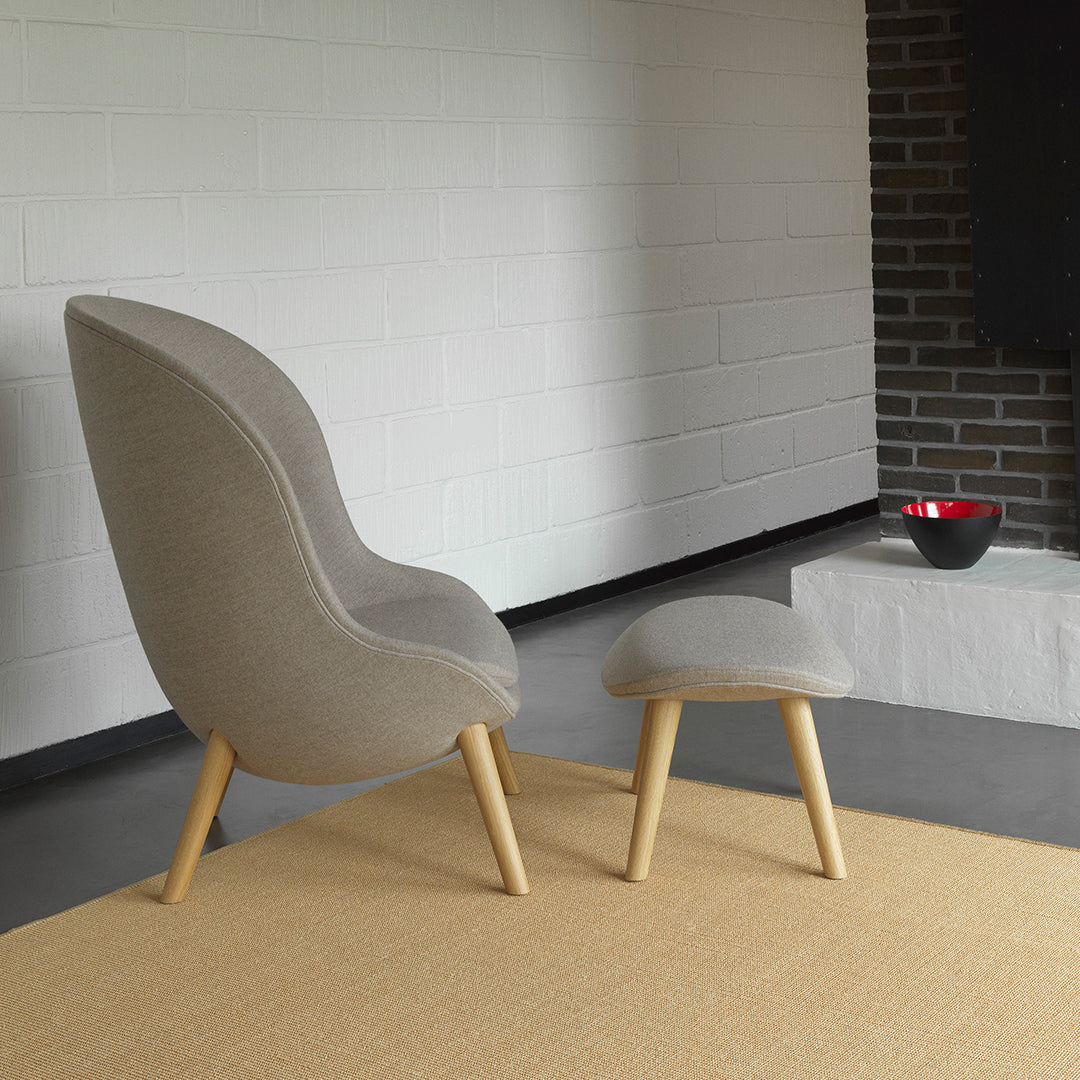Gray upholstered chair with wooden legs and matching ottoman on a light beige rug. Modern minimalist design.