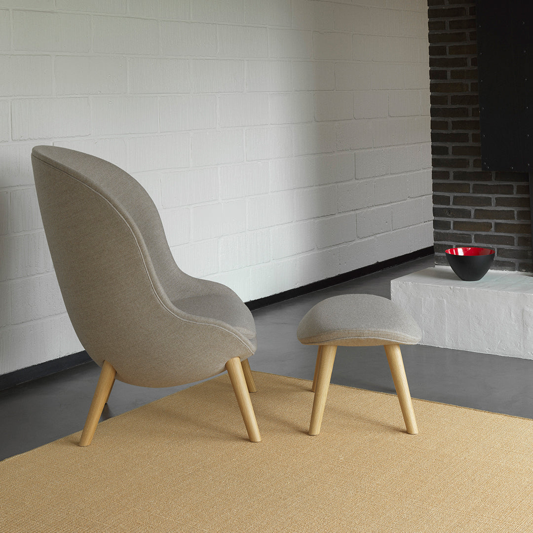 Gray upholstered chair with light wood legs, complemented by a matching footstool on a beige rug. Modern minimalist design.