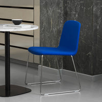Vibrant blue chair with a sleek, minimalist design, paired with a circular marble table on a gray floor.