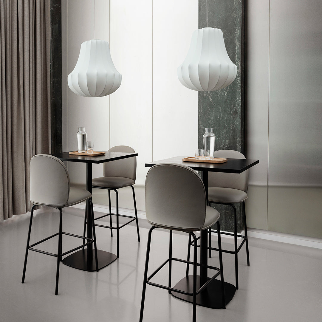 Modern dining setup with sleek black and gray chairs, light wood tables, and elegant white lamps against a neutral backdrop.