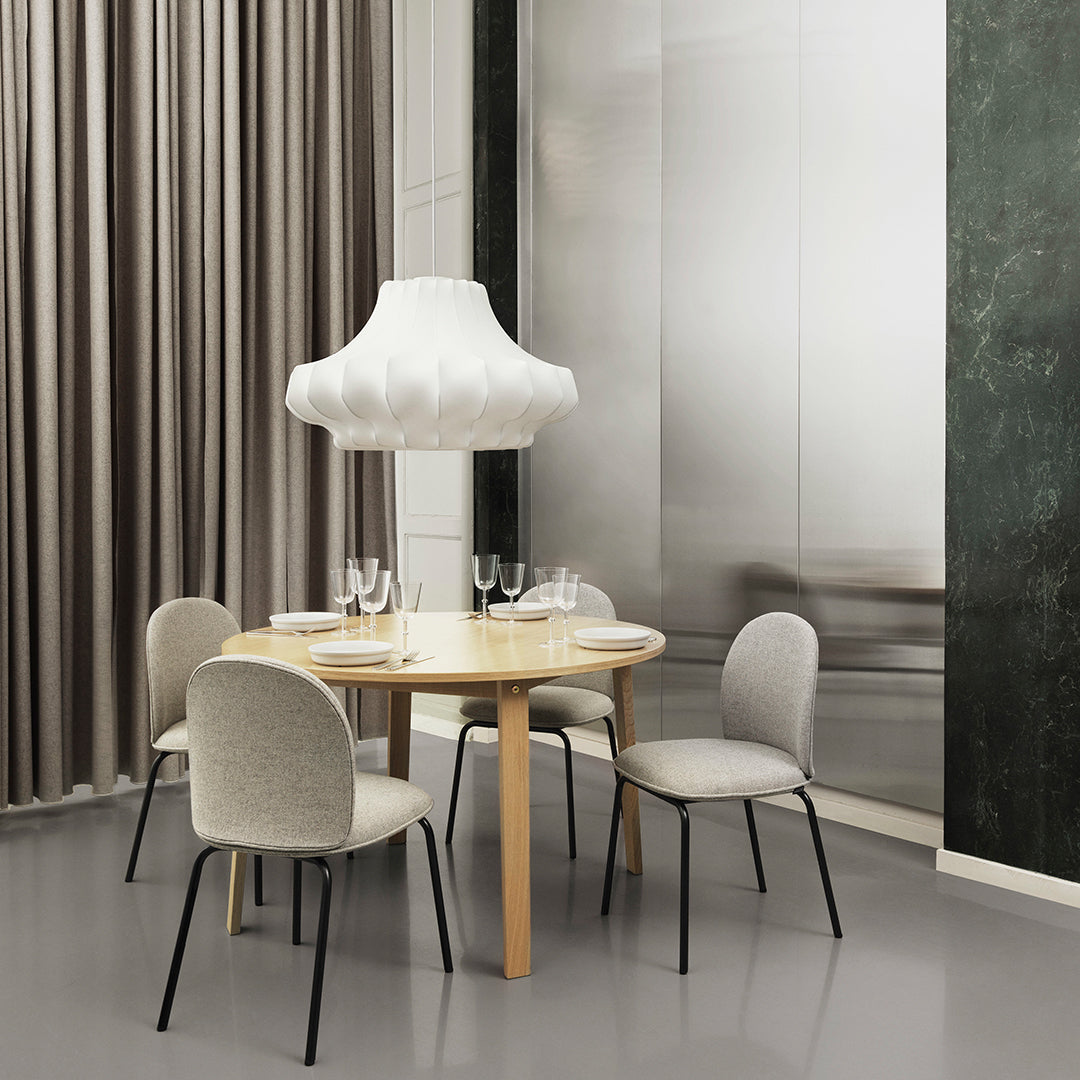 Light wood dining table with gray upholstered chairs and a white pendant lamp, set against neutral tones and textured patterns.