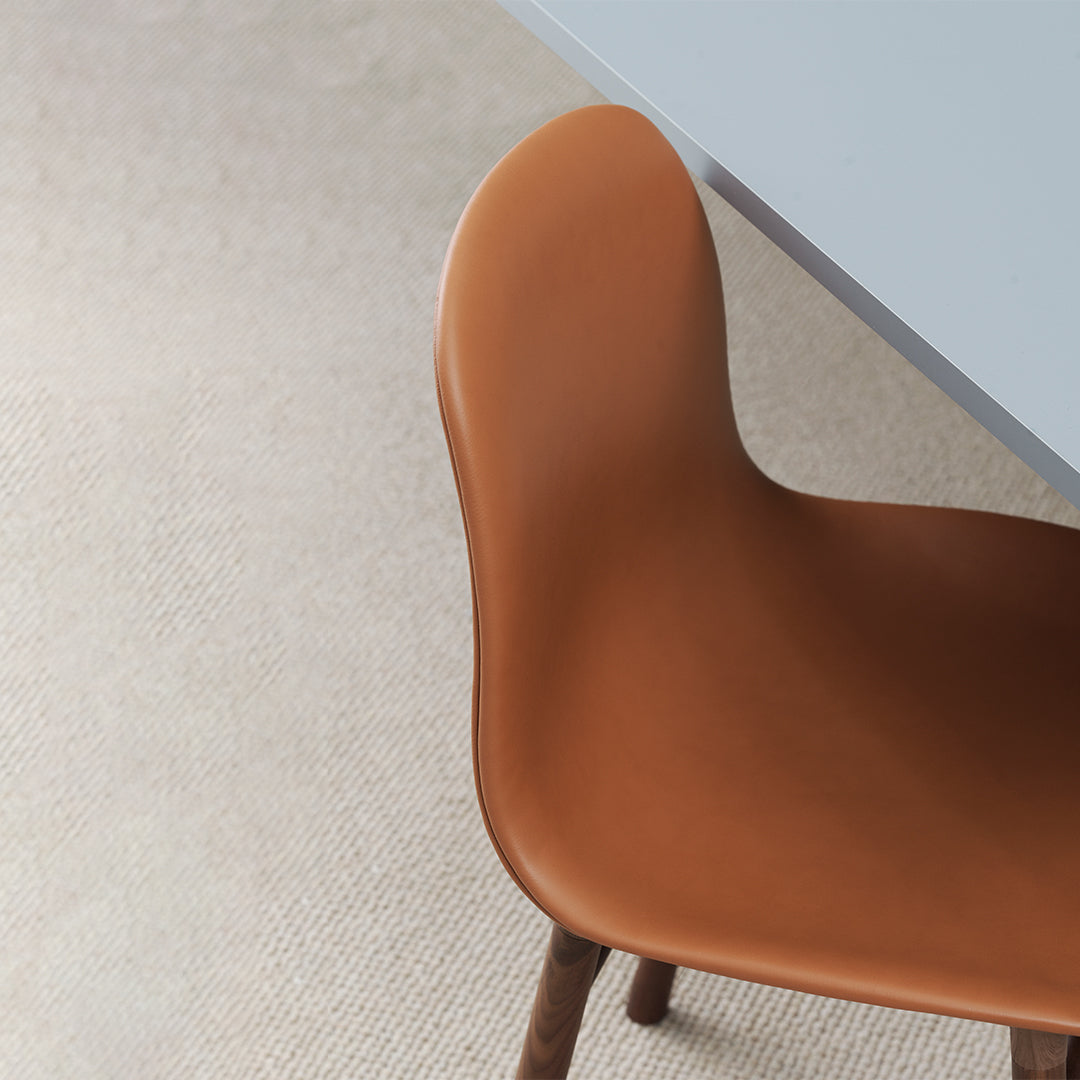 Brown leather chair against a neutral, textured carpet and light blue table. Modern and minimalistic design.
