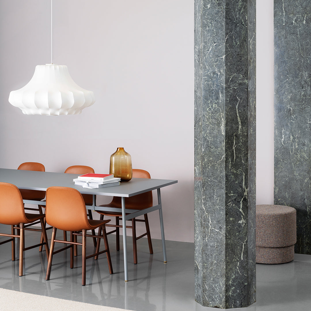 Modern dining room with grey table, orange chairs, marble columns, and soft blush wall. Elegant and stylish color palette.