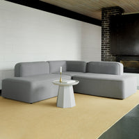 Modern gray sectional sofa with smooth fabric, paired with a geometric white side table on a light beige rug.
