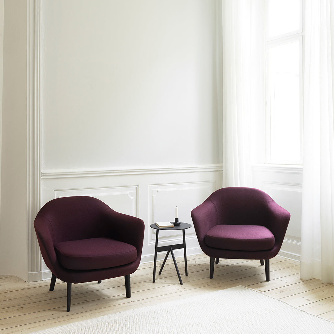 "Two deep burgundy chairs with smooth upholstery, paired with a minimalist black side table in a bright, airy room."