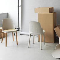 "Modern white chairs with natural wood legs against a neutral backdrop, complemented by cardboard boxes."