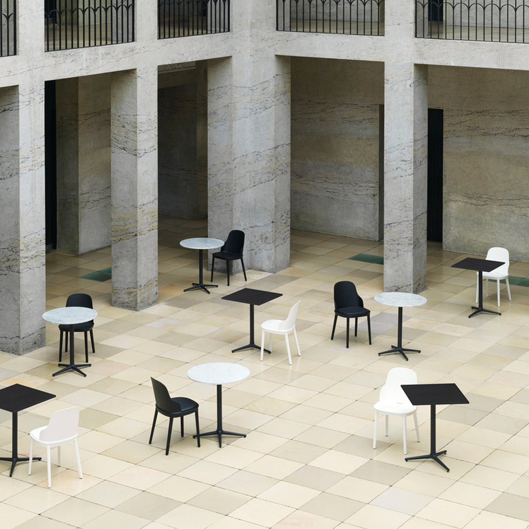 Outdoor café setting with black, white, and gray chairs and tables arranged on a light beige tiled floor.