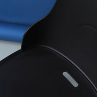 Black chair with smooth curves, set against a vibrant blue background. Minimalist design with sleek lines.
