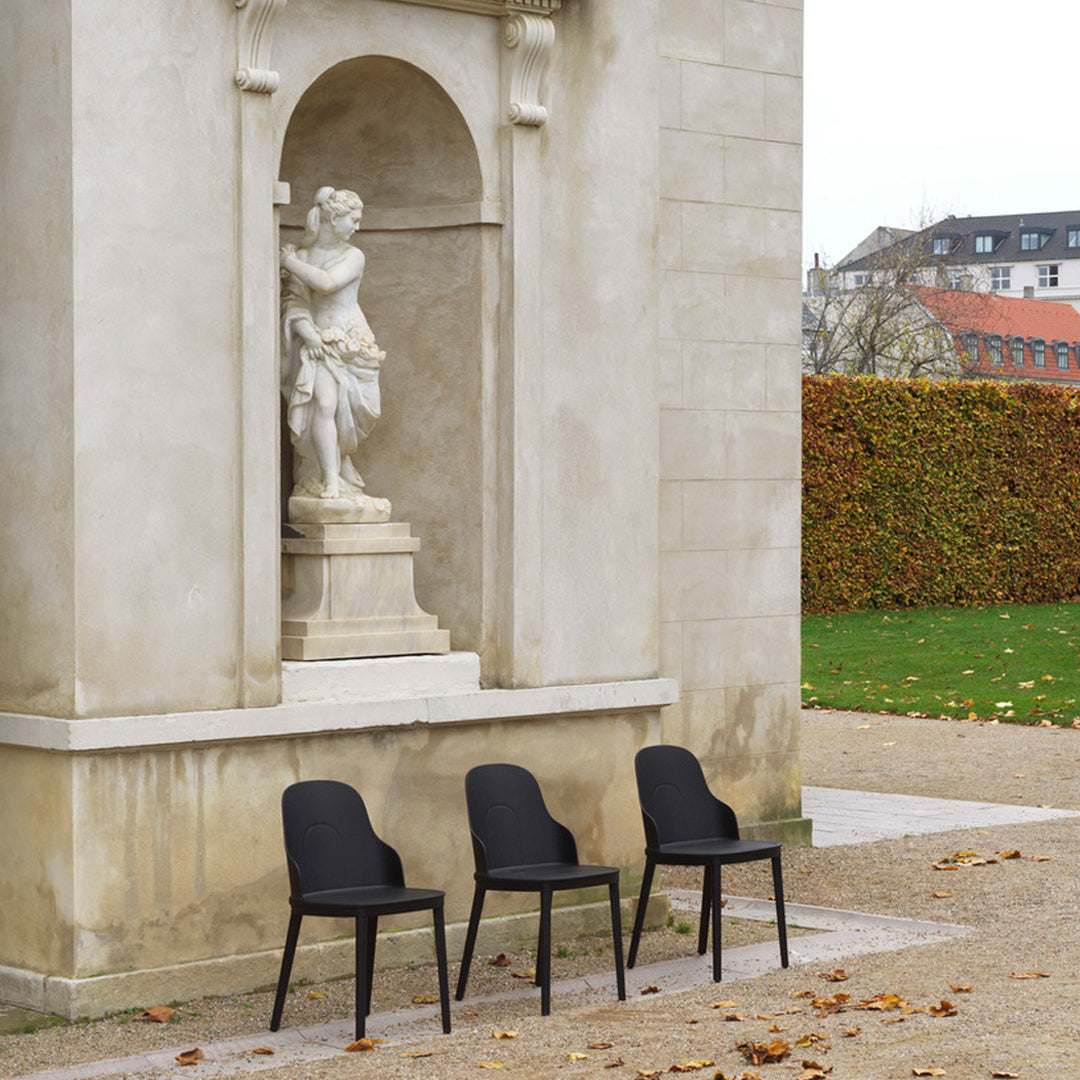 Set of three sleek black chairs against a neutral stone backdrop with vibrant autumn foliage.