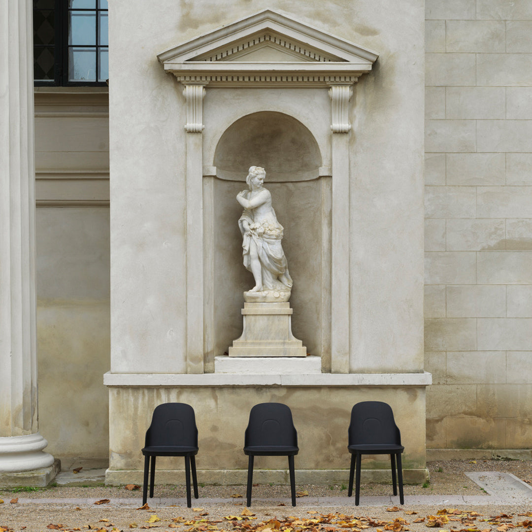 Three sleek black chairs with minimalist design against a neutral, textured stone backdrop.