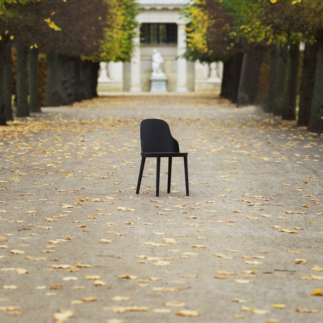 Black modern chair set against a tranquil pathway adorned with autumn leaves, featuring golden yellow and muted earth tones.