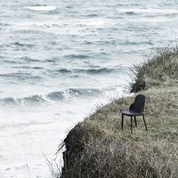 Black minimalist chair against a tranquil ocean backdrop, featuring muted tones of gray and green grass.
