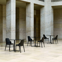 Black chairs with sleek designs around glass-topped tables on a light beige stone floor with subtle marble patterns.