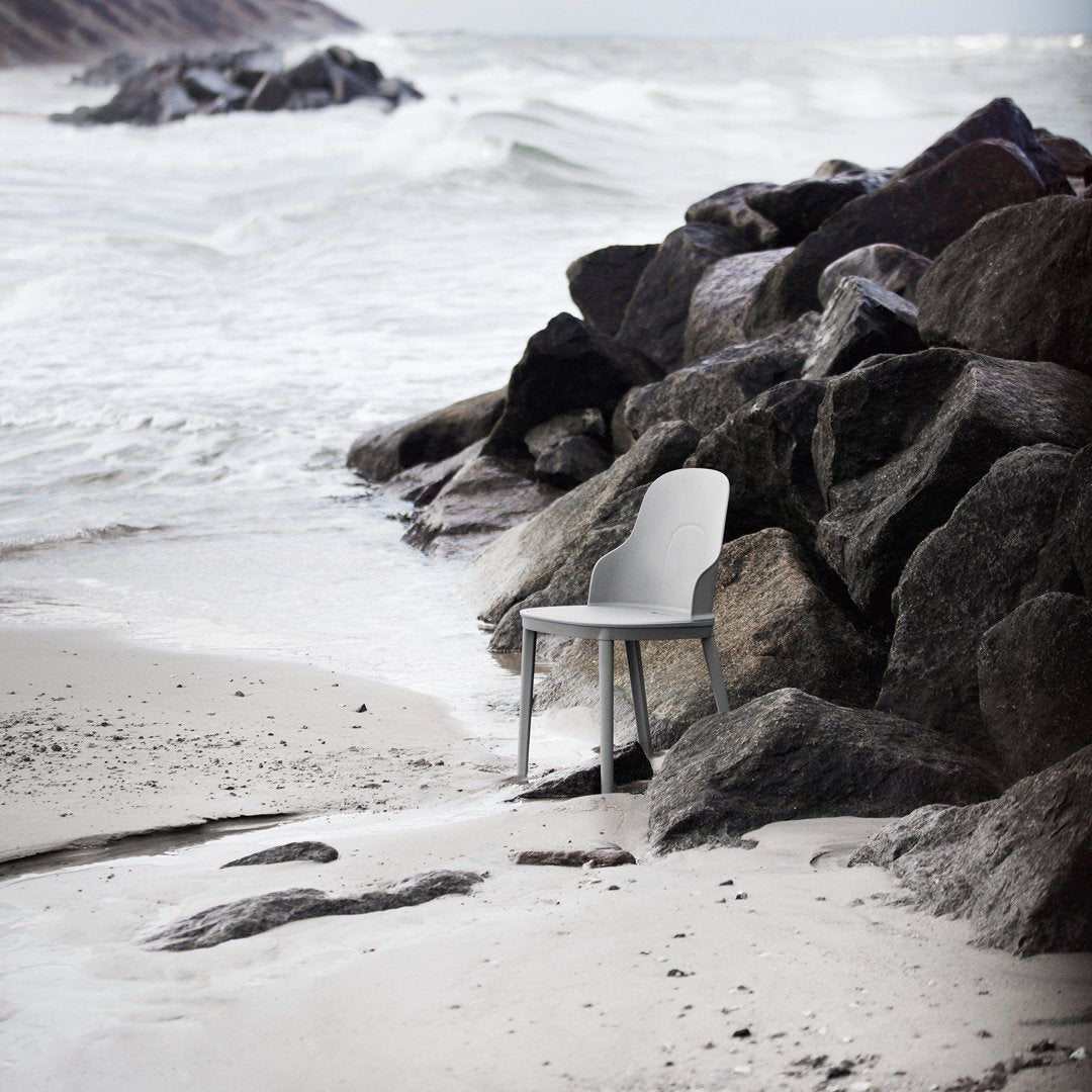 White chair with smooth, modern design contrasting against rough, dark rocks and rippling ocean waves.