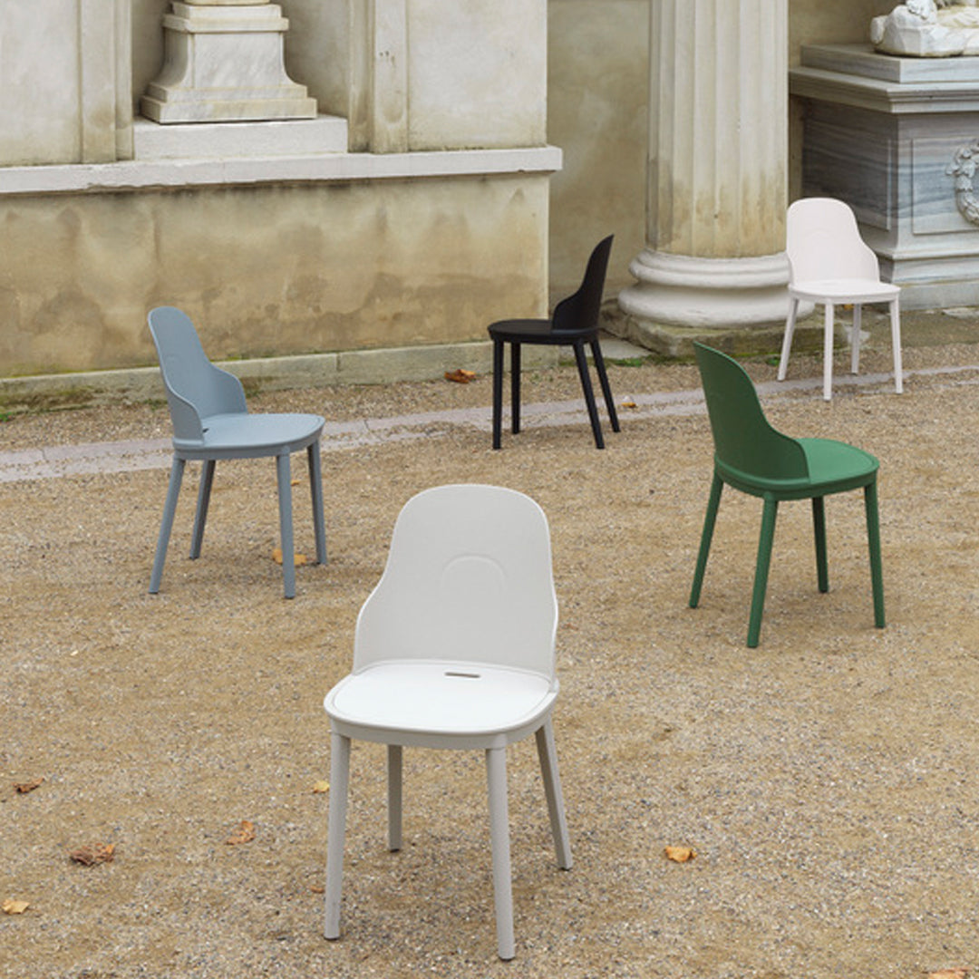 Five contemporary chairs in pastel shades of gray, green, blue, and black, set against a textured gravel background.