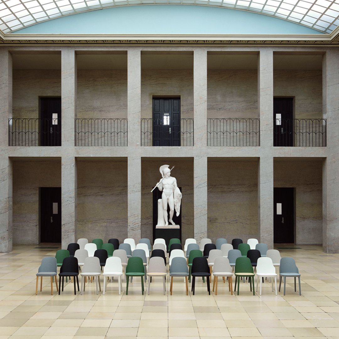 Colorful chairs in green, white, gray, and black arranged artfully in a spacious gallery setting.