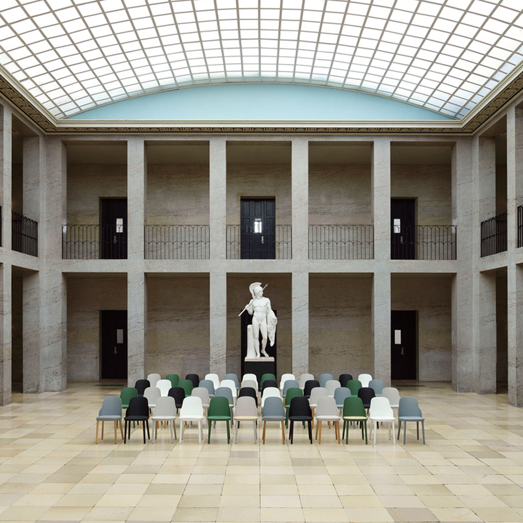 Colorful seating arrangement with green, grey, and black chairs in a modern gallery setting, featuring stone and glass architecture.