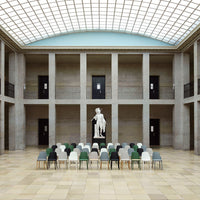 Colorful seating arrangement with green, grey, and black chairs in a modern gallery setting, featuring stone and glass architecture.
