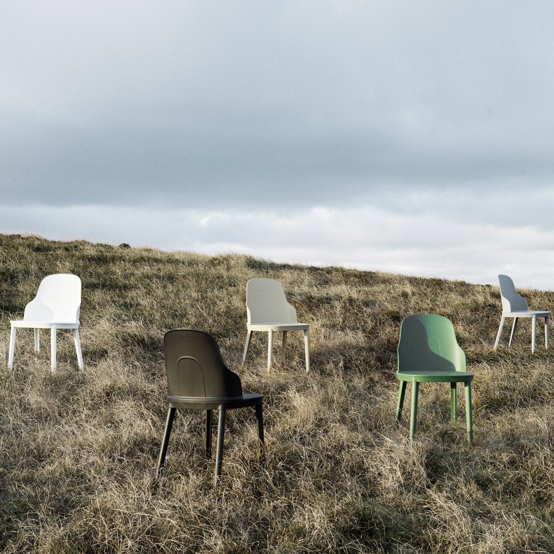 "Colorful chairs in white, green, gray, and black set against a natural grass landscape under a cloudy sky."
