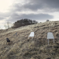 Minimalist outdoor chairs in black, grey, and white set against a grassy hillside under a cloudy sky.