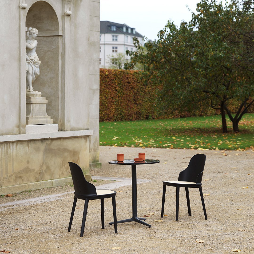 Black dining chairs around a sleek round table in a serene outdoor setting, featuring muted earth tones and greenery.