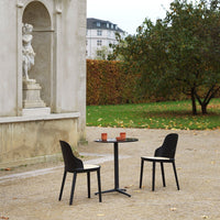 Black dining chairs around a sleek round table in a serene outdoor setting, featuring muted earth tones and greenery.