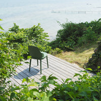 Green outdoor chair on a wooden deck, surrounded by lush greenery and a tranquil water view.
